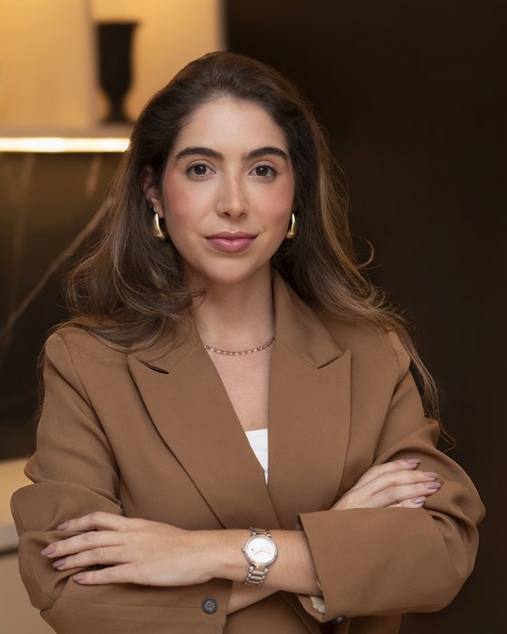 Retrato da Dra. Débora Guedes, cirurgiã-dentista, de braços cruzados em ambiente de consultório.